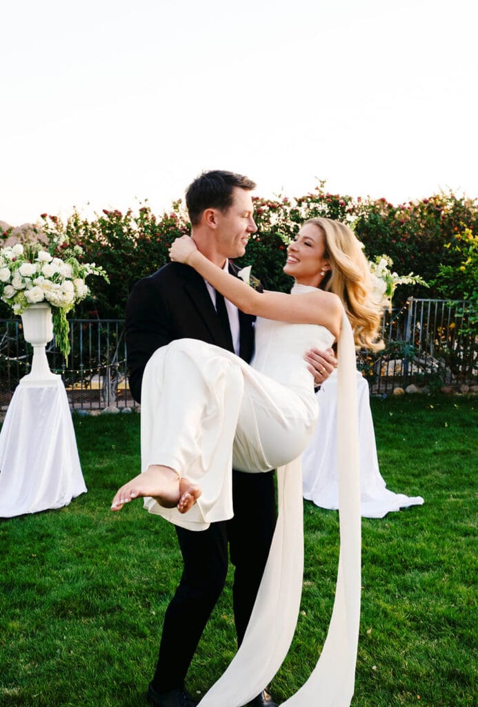 Groom carrying the bride across the lawn after their outdoor Airbnb wedding ceremony.
