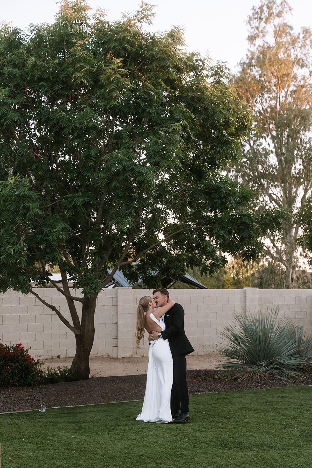 Bride and groom kissing on the lawn during their backyard Airbnb wedding celebration.