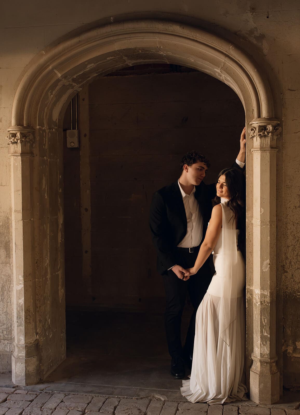 Bride and groom holding hands beneath an intricately carved stone doorway.