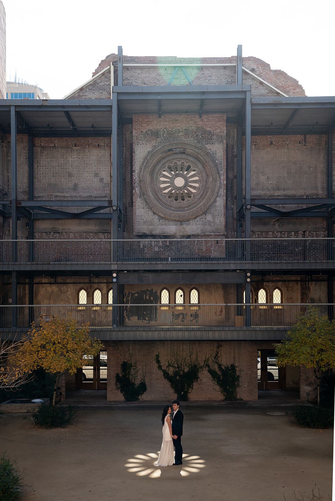 Couple posing in the courtyard beneath the ornate facade of a historic industrial venue.