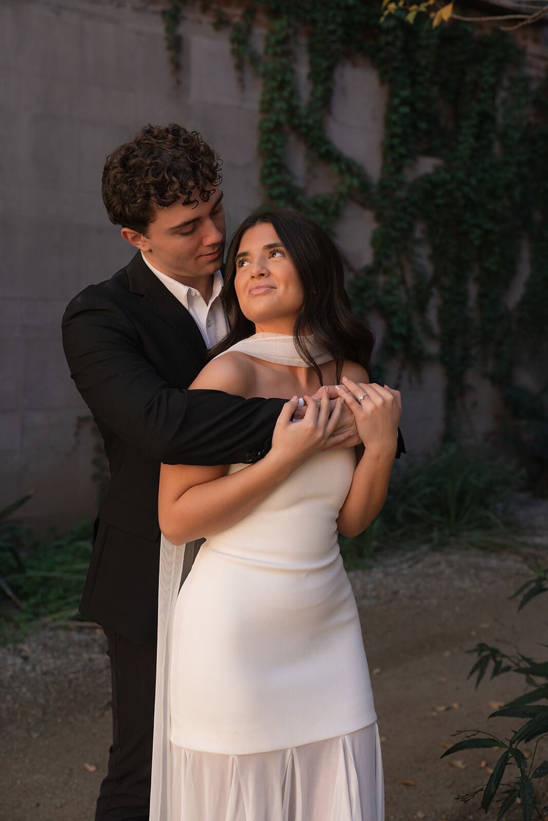 Couple embracing during a softly lit wedding portrait beside an ivy-covered wall.