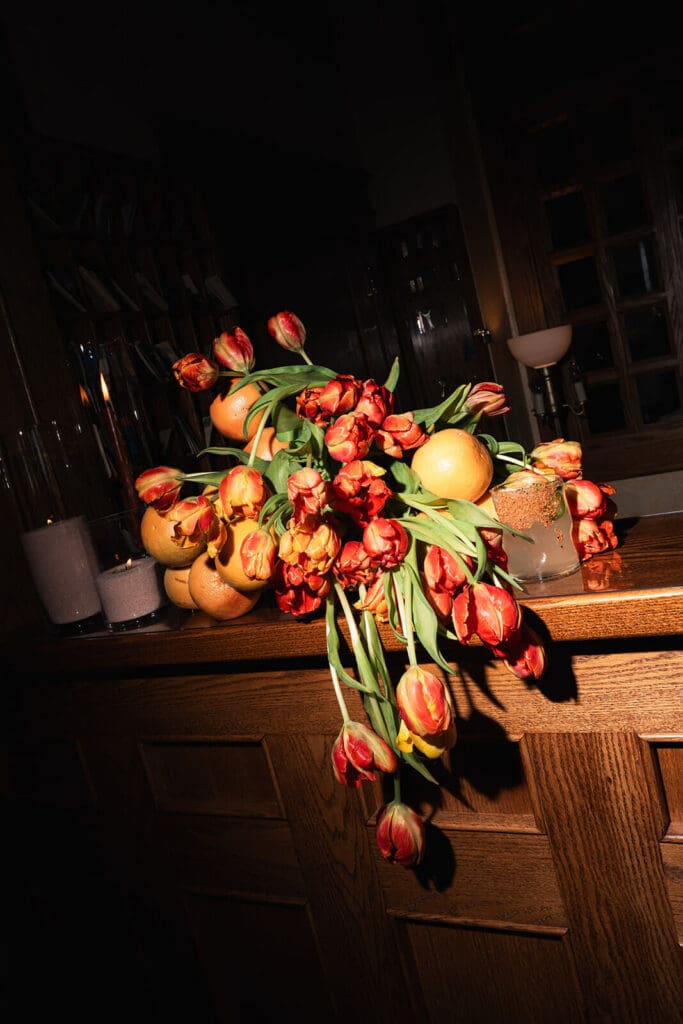 Colorful orange and red wedding flowers arranged on a dark wooden table inside the reception space.