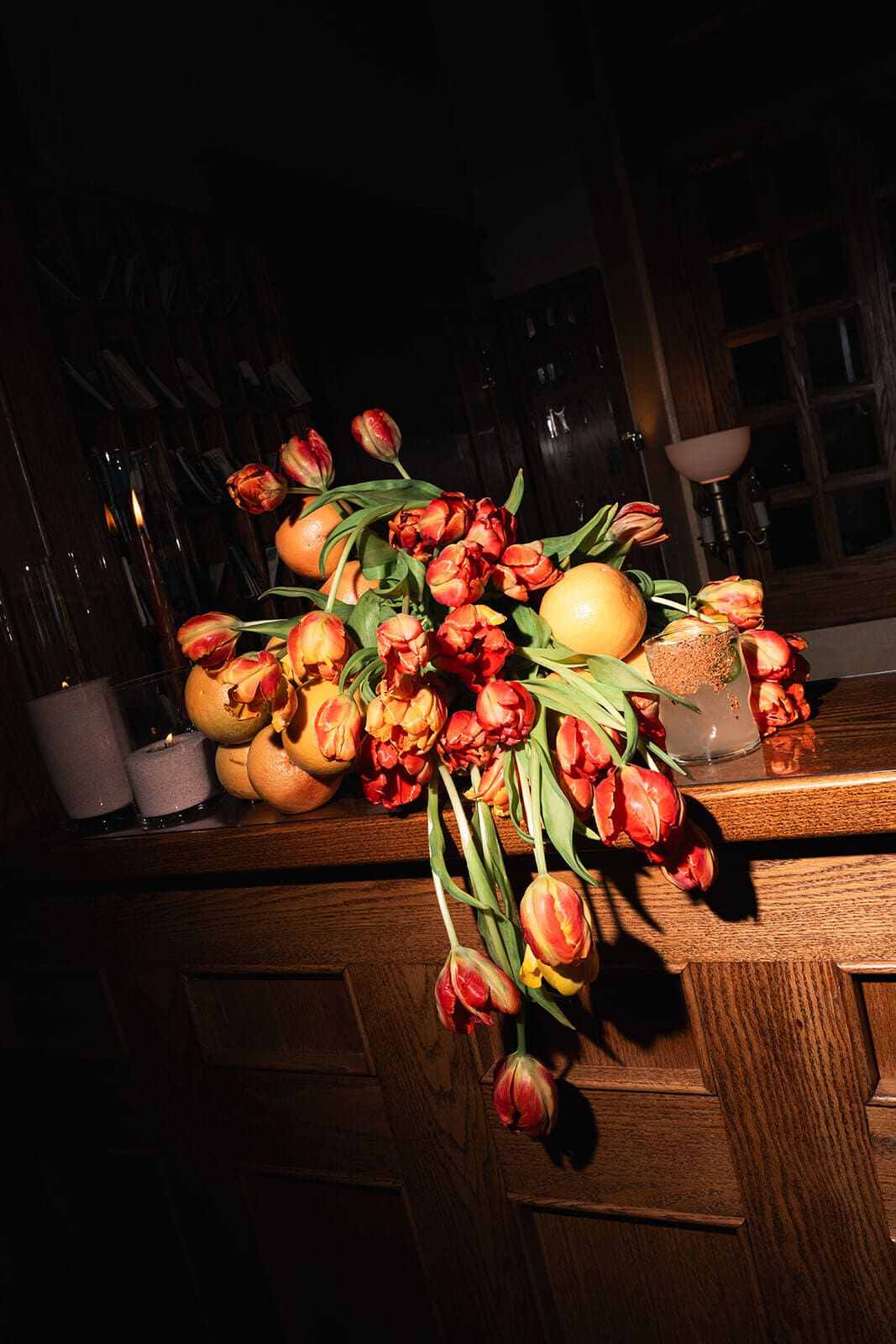 Dramatic wedding floral arrangement featuring citrus fruit and warm-toned flowers in low light.