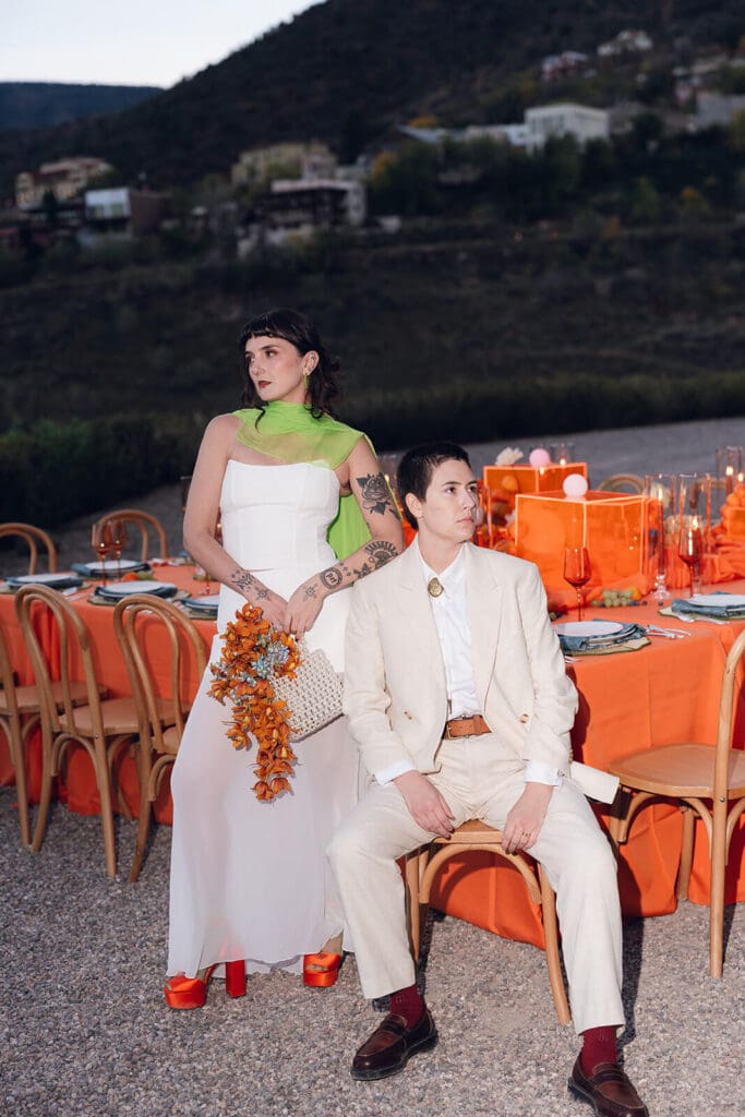 Newlyweds posing beside vivid orange reception tables with mountains rising behind the outdoor celebration.