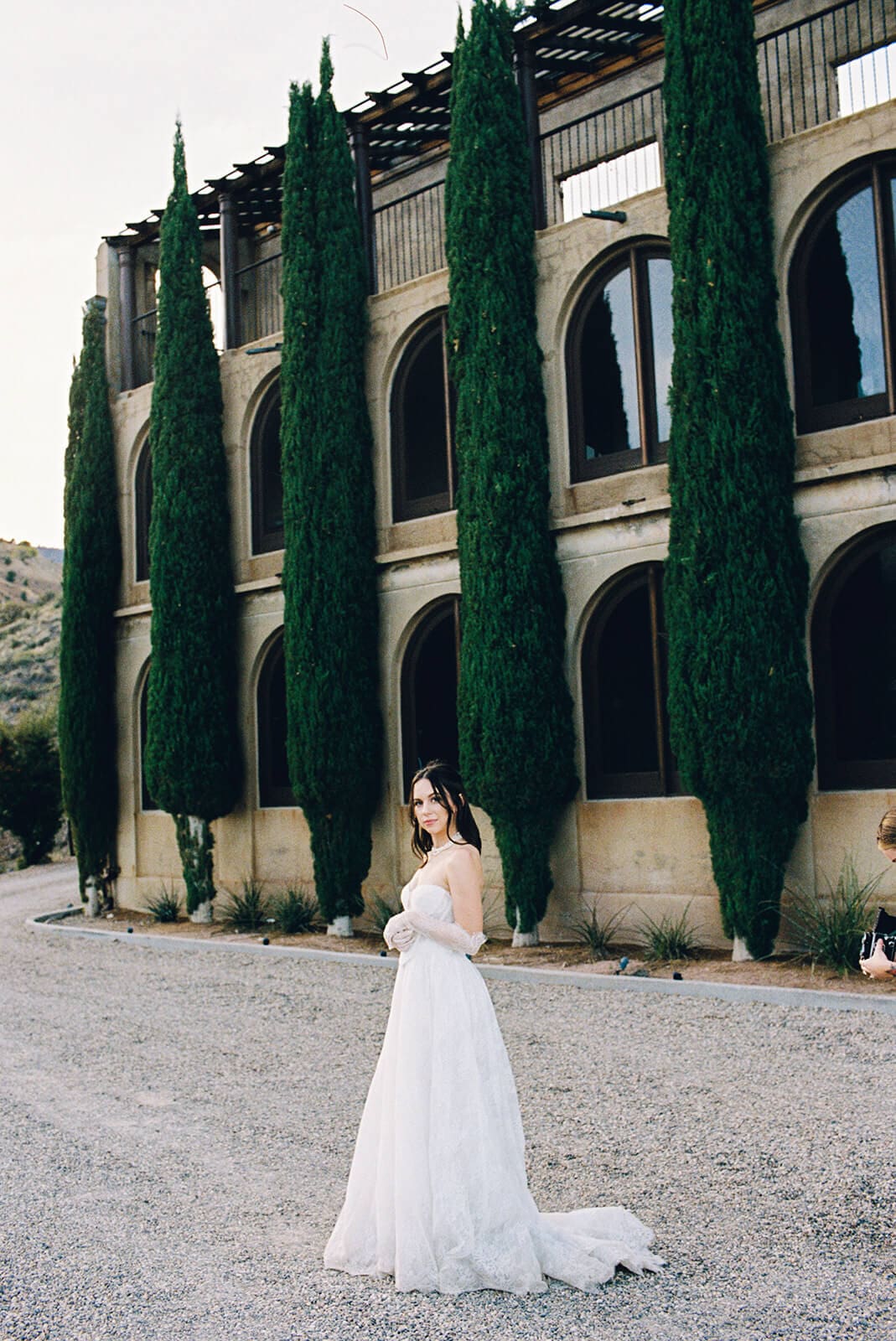 Bride posing beside tall cypress trees and historic architecture at an Arizona wedding venue.