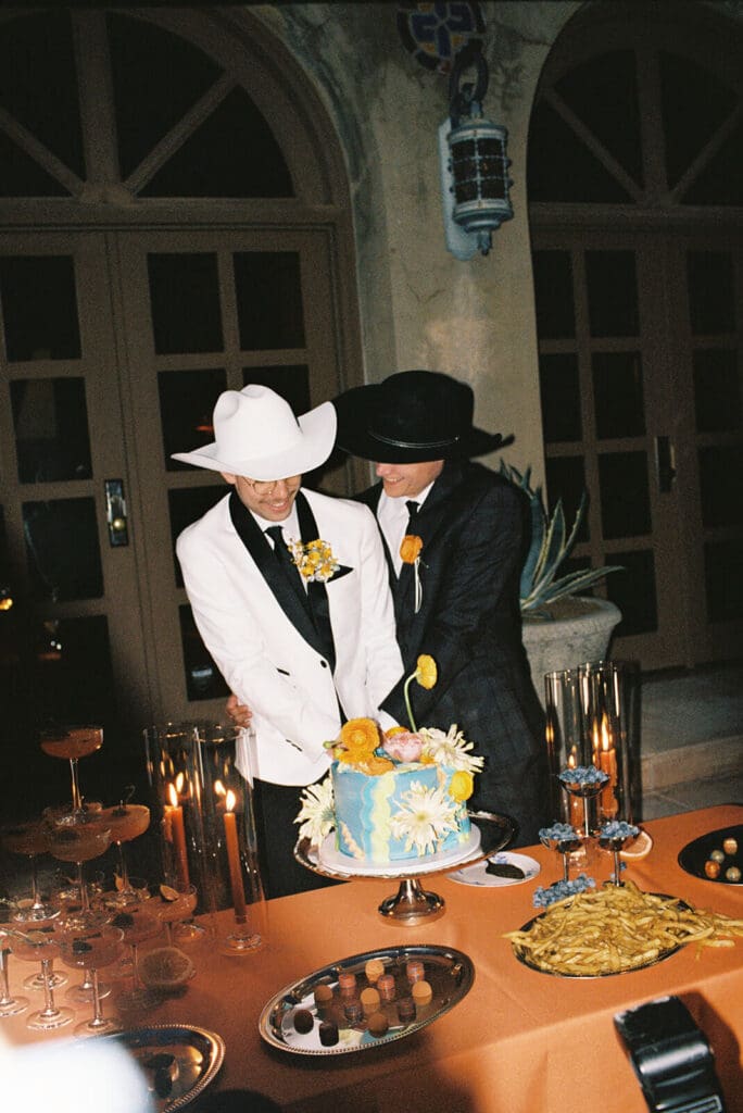 Newlyweds wearing cowboy hats while cutting a colorful wedding cake at their reception.