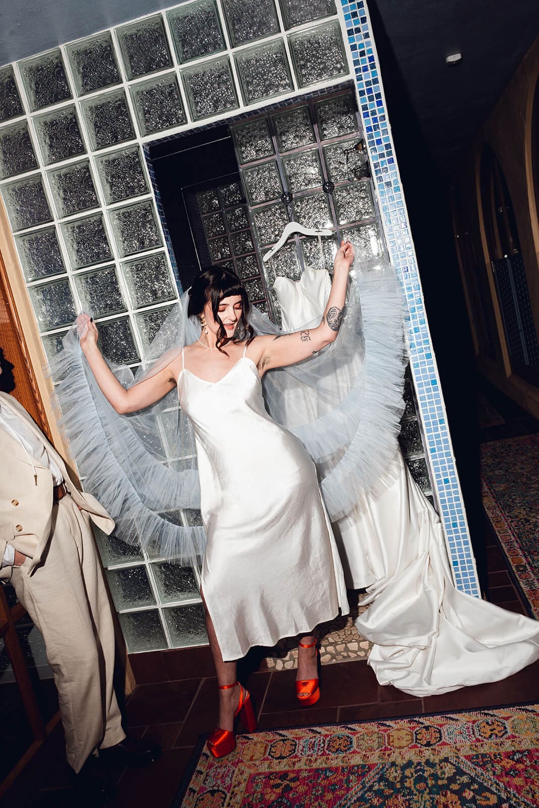 Bride dancing solo in the glass block doorway, arms raised, her tulle veil swirling around her
