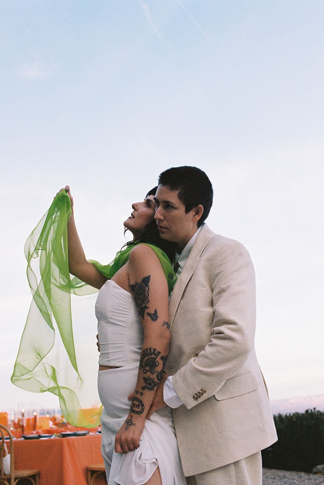 Couple embracing outdoors as her lime green sash blows sideways in the wind

