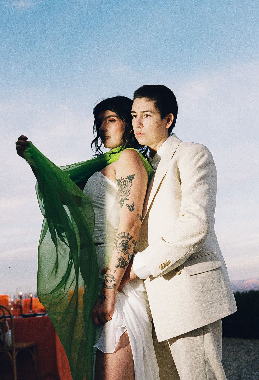 Couple standing together at dusk, her green sash caught mid-flutter in the wind at The Little Daisy wedding venue

