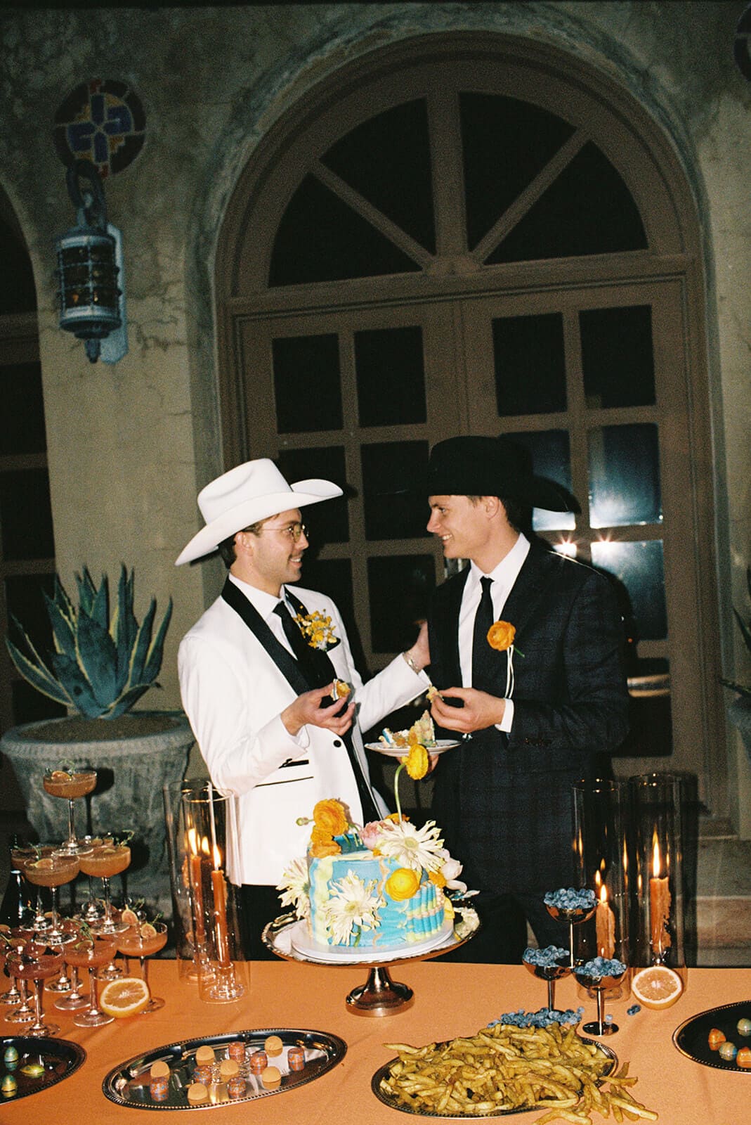 Two grooms cutting a colorful wedding cake during their reception.