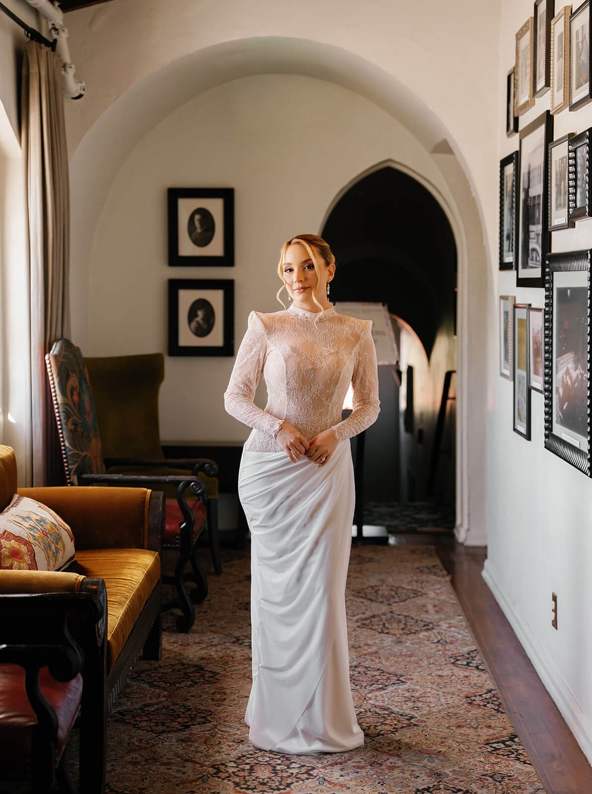 Bride showing the lace back of her fitted wedding dress inside an arched sitting room.