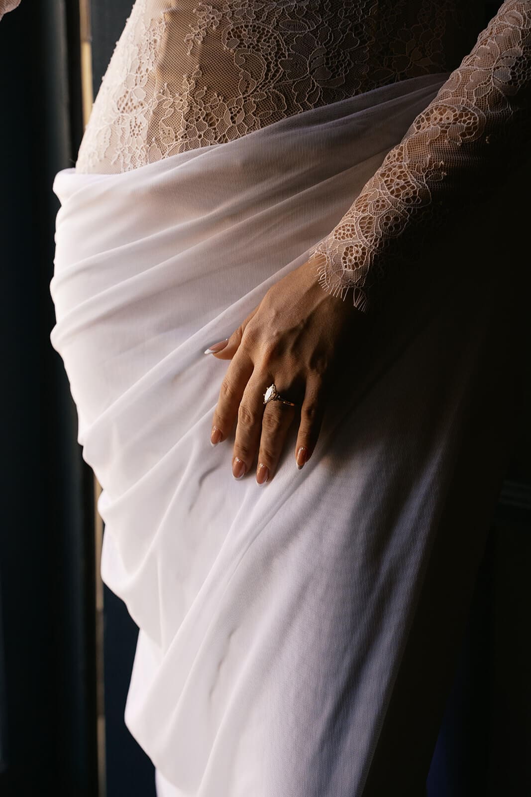 Close-up of a bride’s hand gathering the flowing fabric of her wedding dress.