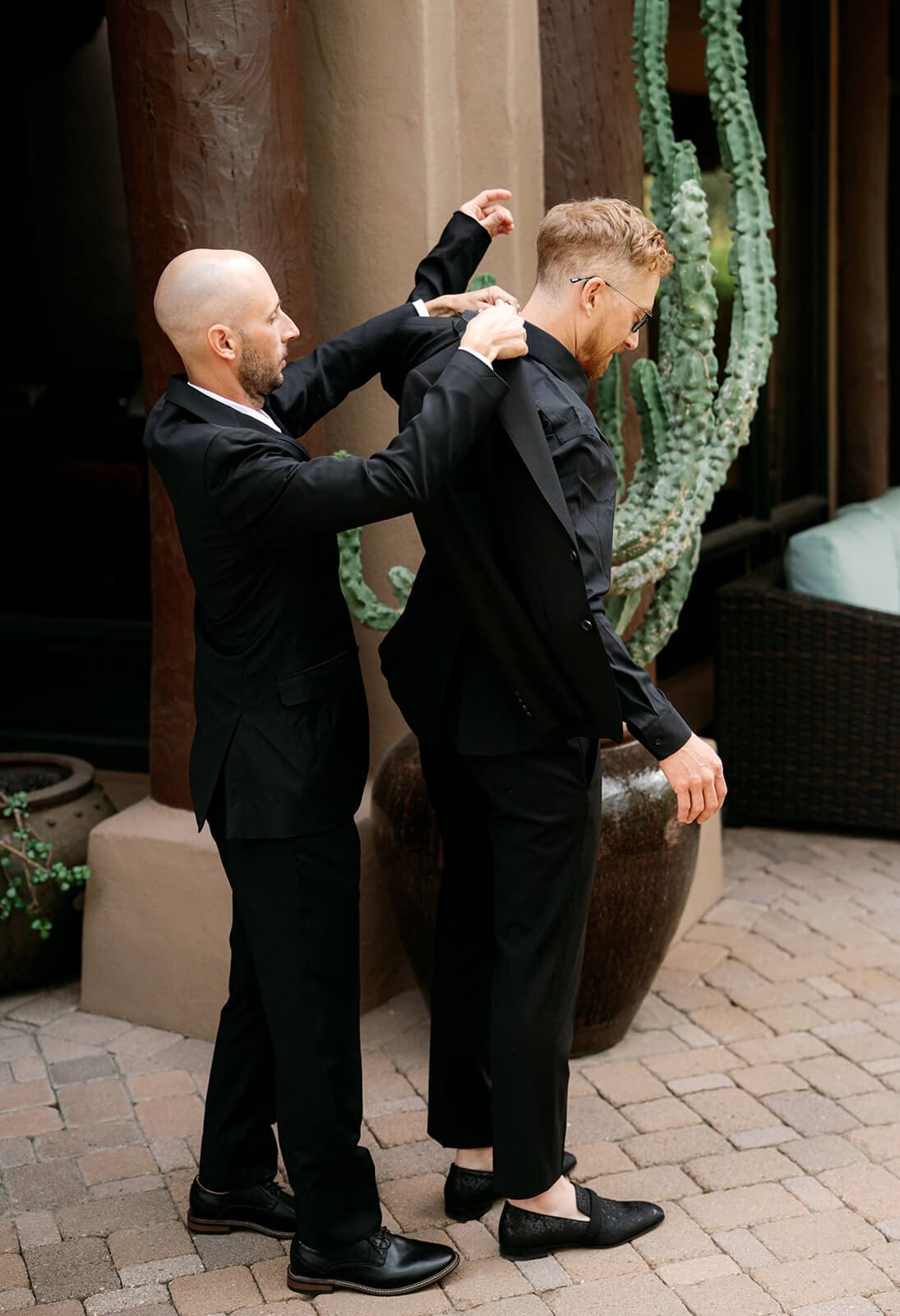 Groomsman helping the groom adjust his black wedding suit before the ceremony.