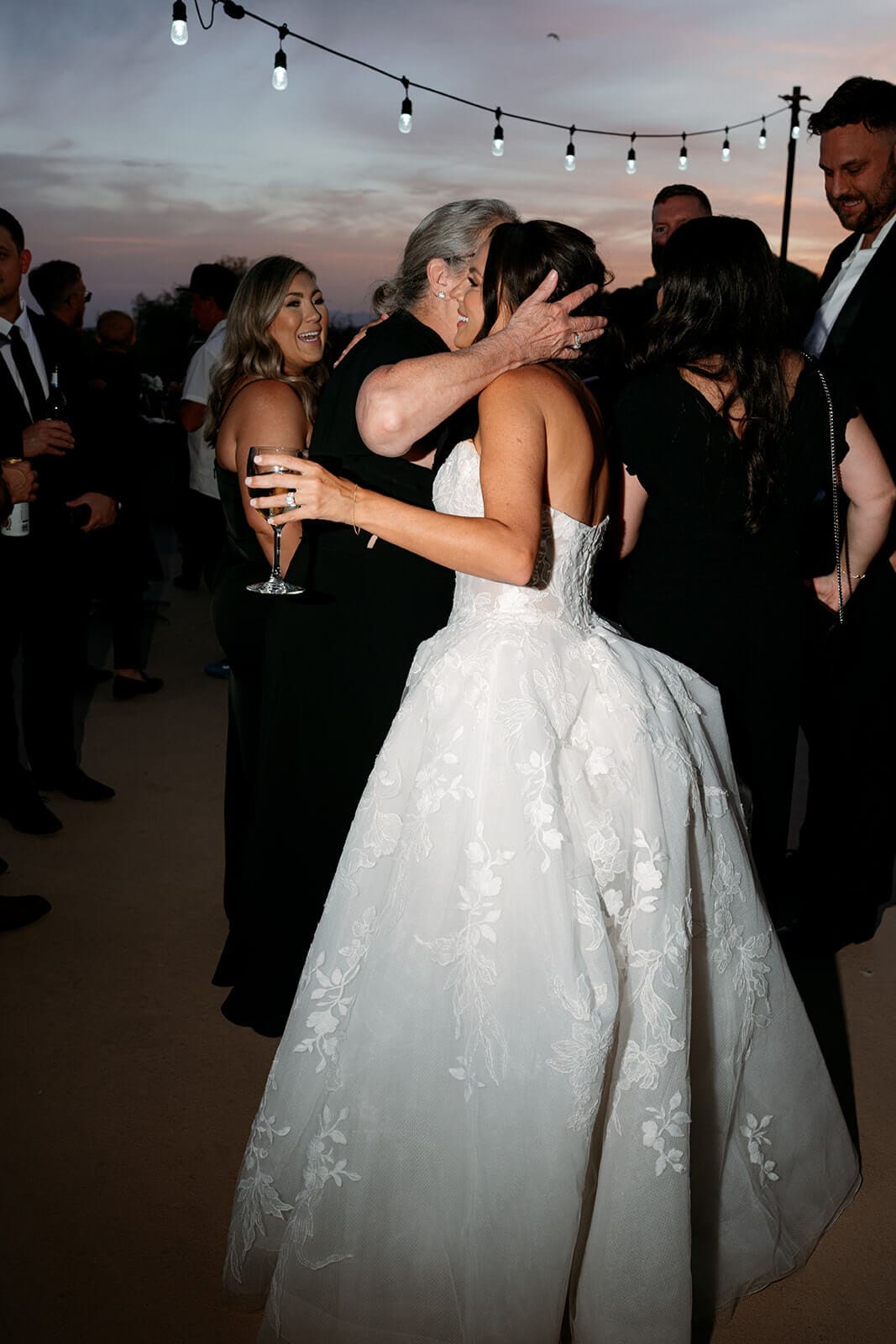 Bride in a lace wedding gown hugging a guest during the outdoor reception.