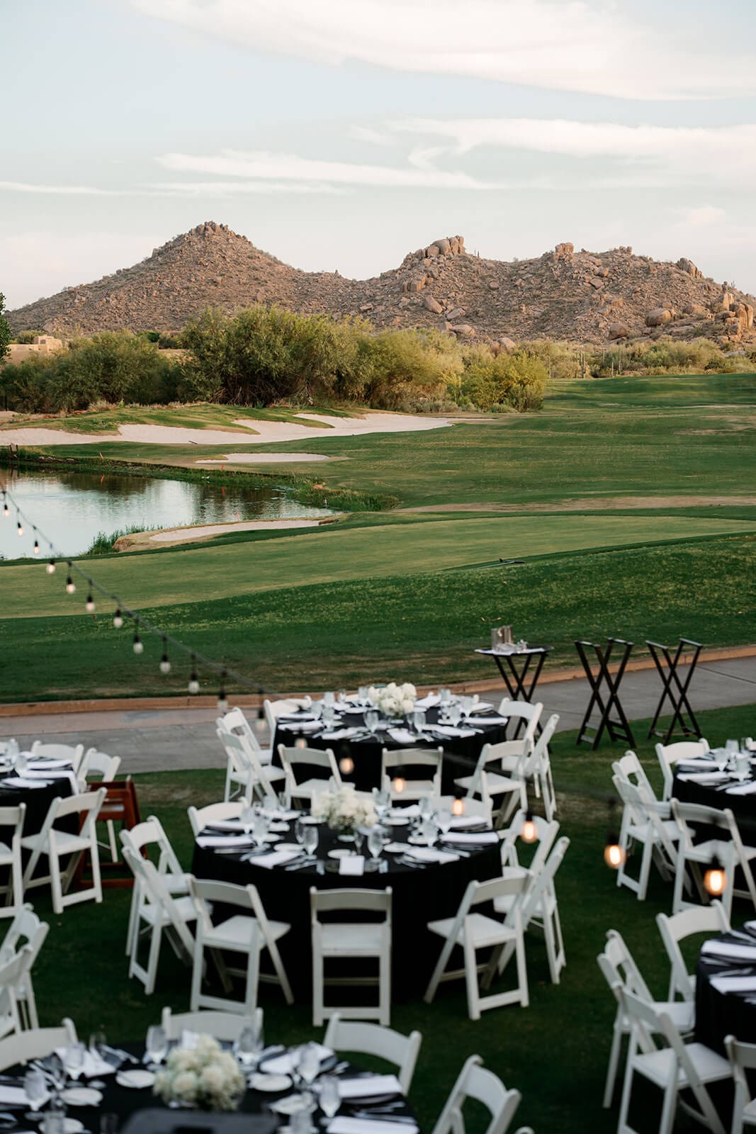 Bride holding hands with a young wedding attendant in a black tuxedo while walking through a desert wedding venue.