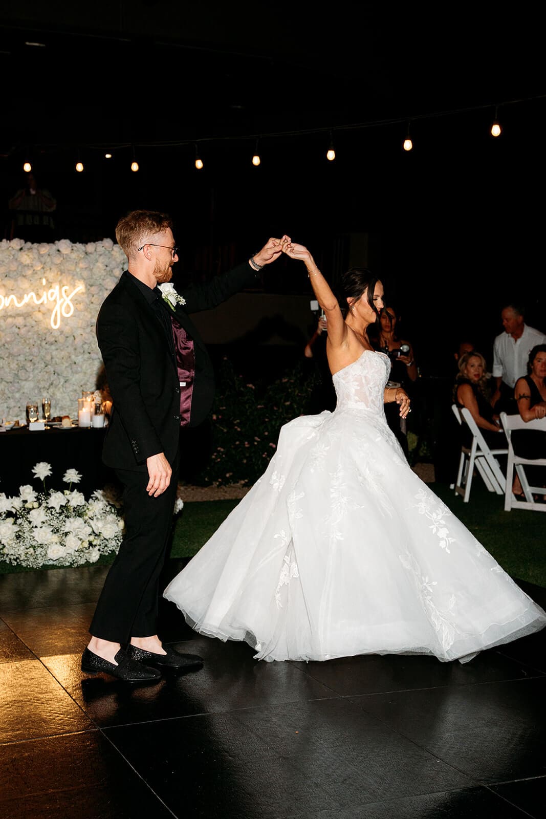 Bride and groom dancing together at their outdoor wedding reception beneath string lights.