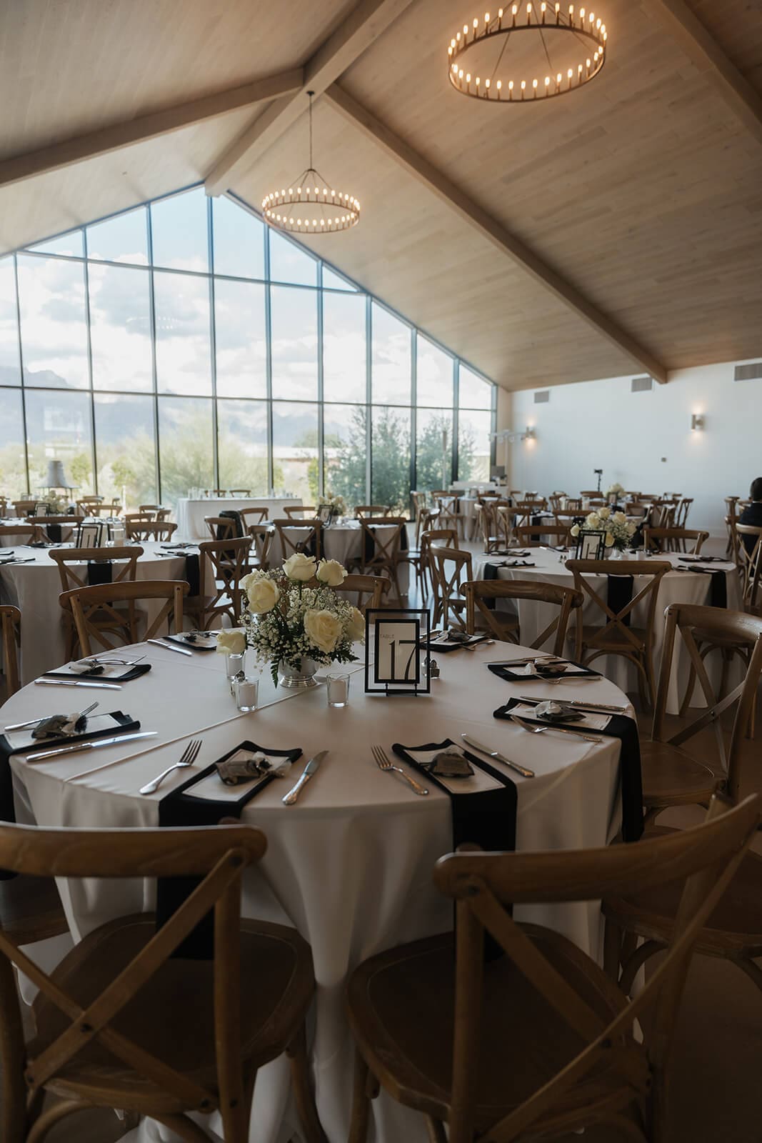 Wedding reception tables arranged inside a bright modern venue with chandeliers, neutral linens, and floor-to-ceiling desert views.