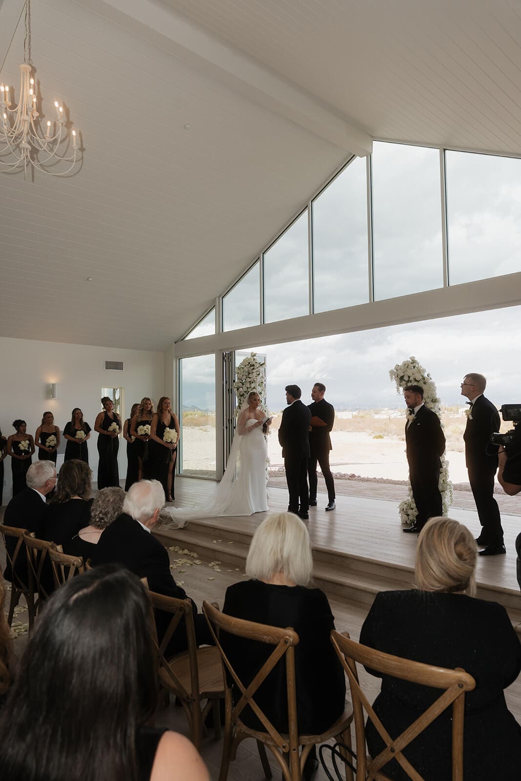 Indoor wedding ceremony inside a bright white venue with floor-to-ceiling windows overlooking the Arizona desert.