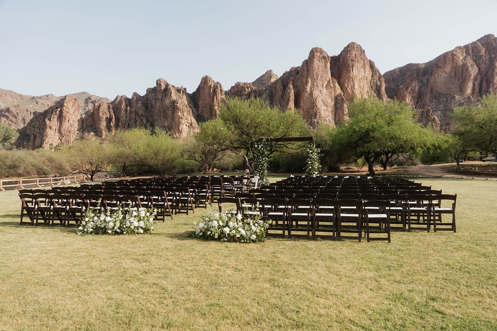 Outdoor wedding ceremony setup with rows of wooden chairs, white floral arrangements, and the Superstition Mountains filling the background.