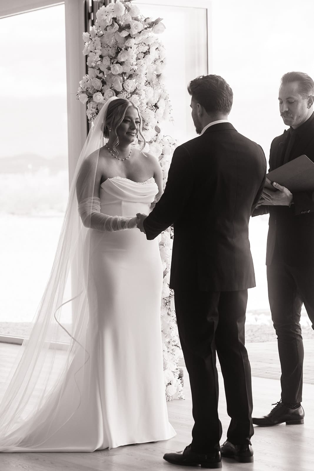 Black-and-white photo of the bride and groom exchanging vows during an intimate indoor wedding ceremony.
