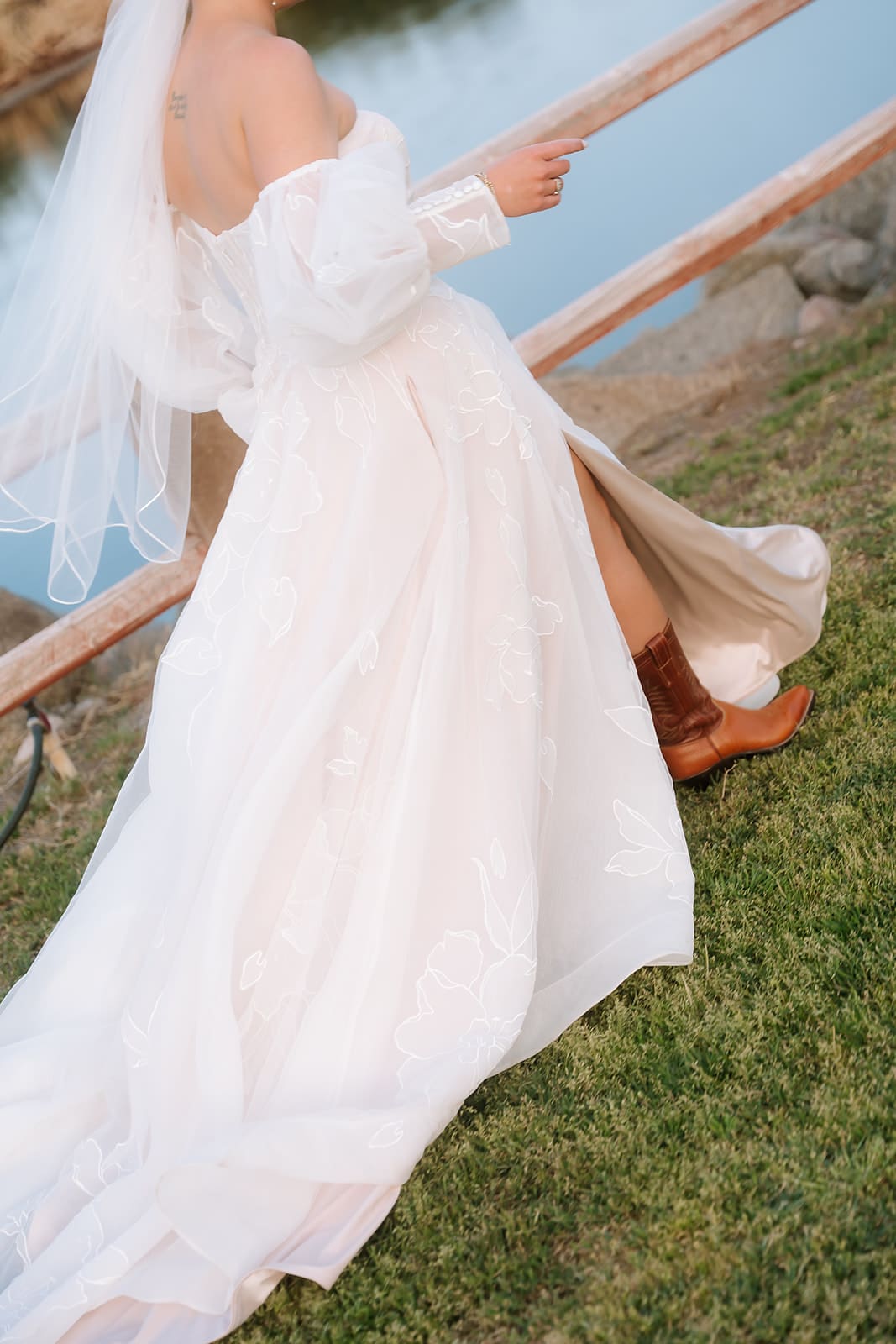 Close-up of a bride lifting her wedding dress while walking, revealing brown western boots beneath her flowing gown.