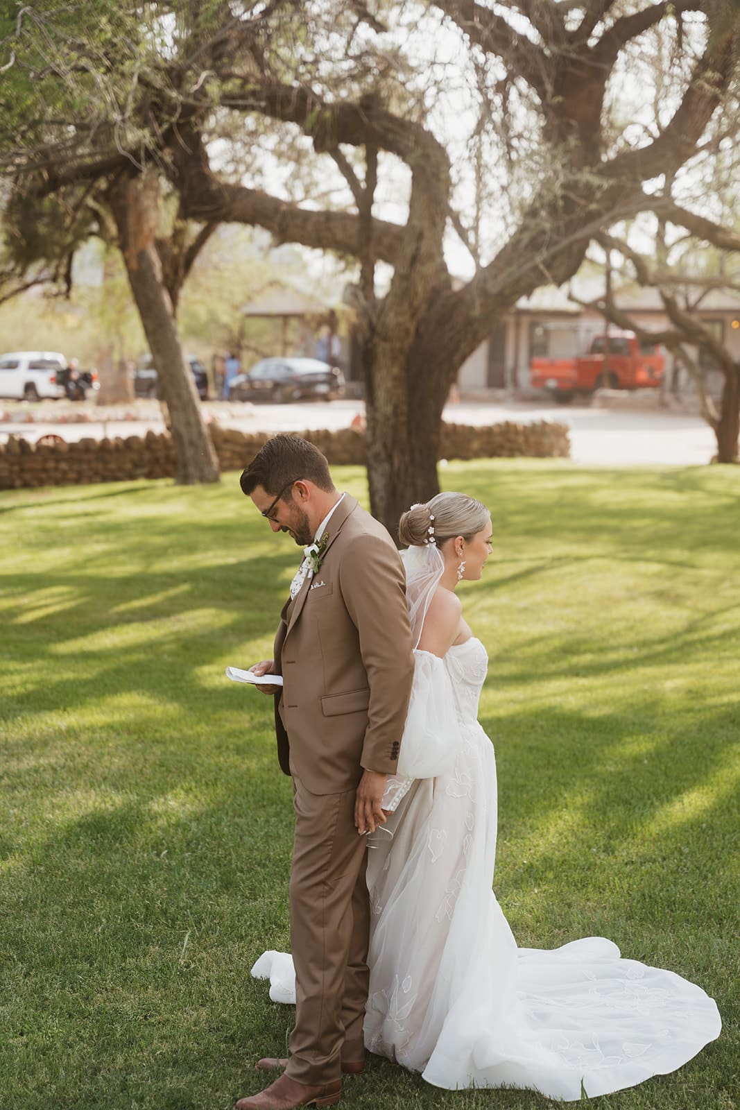 Bride and groom stand back-to-back beneath a large tree during a quiet moment at their Arizona wedding