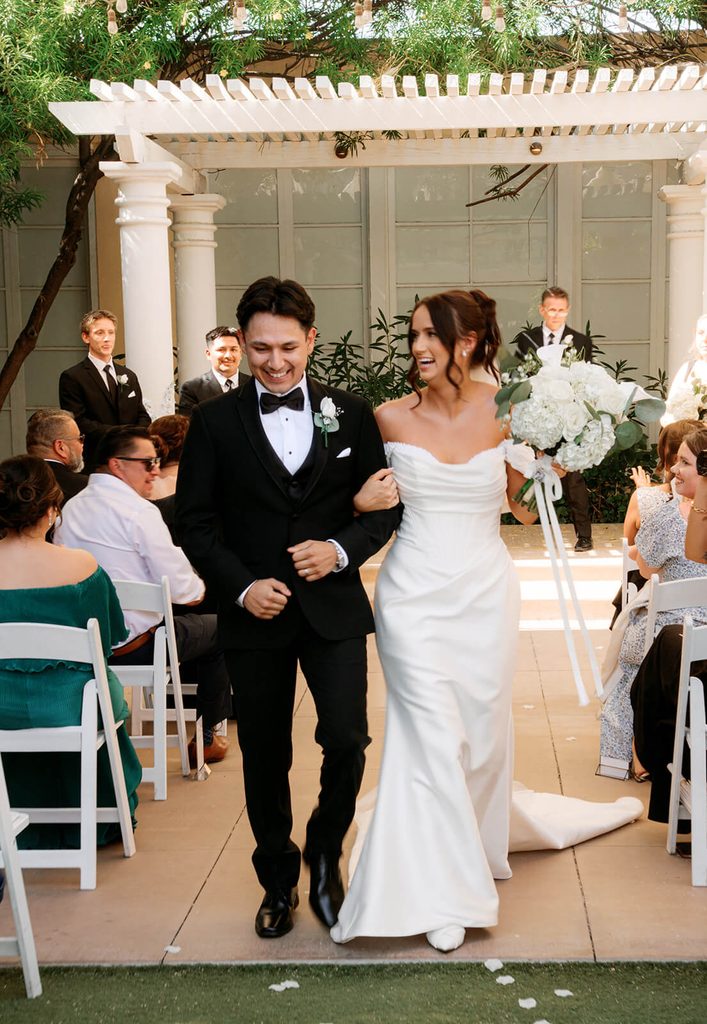 Newlyweds smiling as they walk back down the aisle together after their ceremony.
