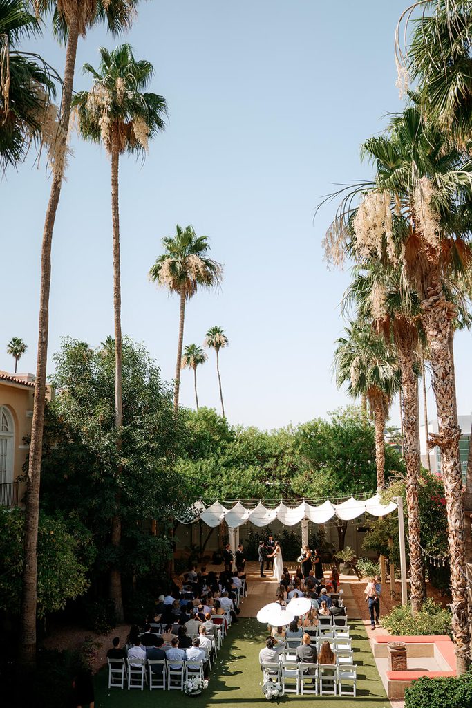 Wide view of an outdoor Arizona wedding ceremony surrounded by tall palm trees and greenery.