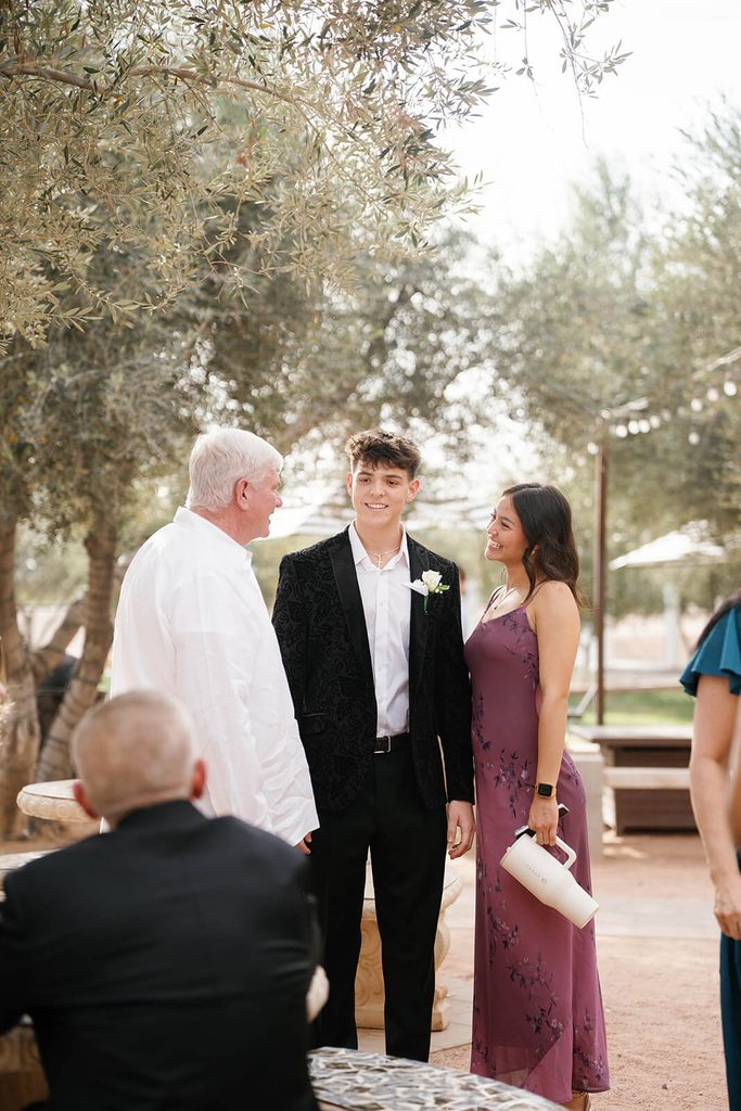Groom posing with a wedding guest beneath the olive trees during the reception.