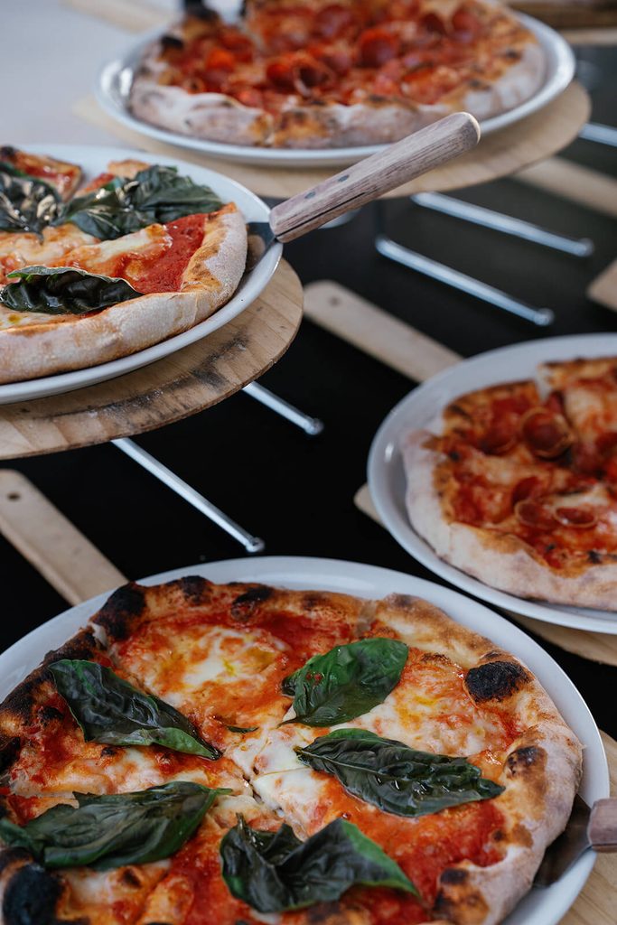 Fresh pizzas topped with basil and other toppings served at a wedding reception.