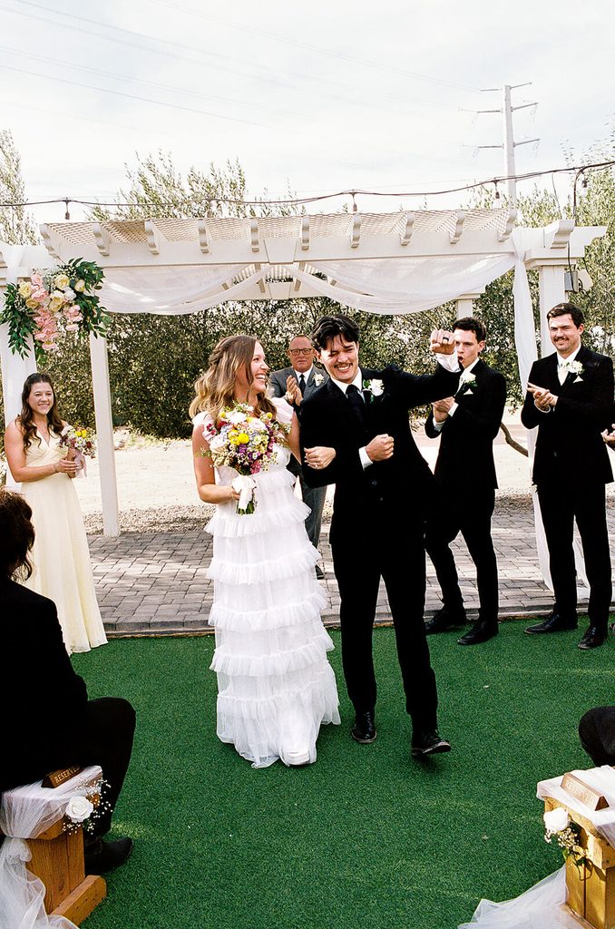 Newlyweds walking back down the aisle while their wedding party cheers behind them.