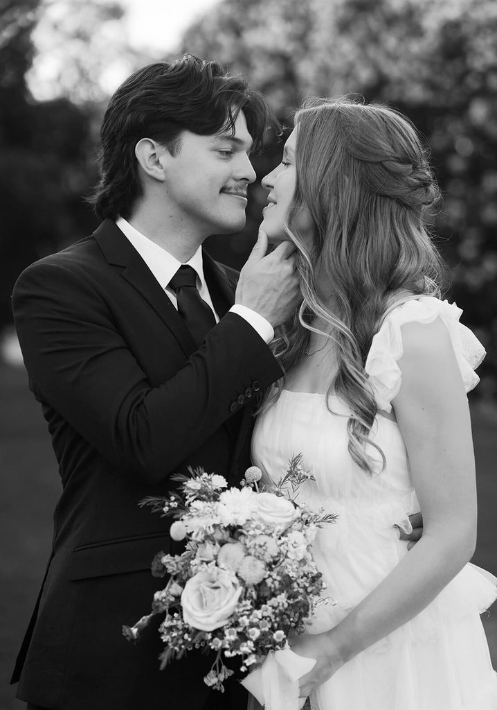 Black-and-white close-up of the bride and groom smiling at each other while holding the bridal bouquet.