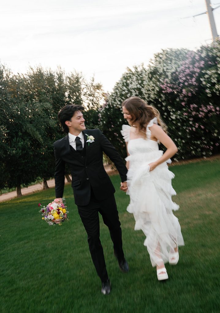 Newlyweds running hand in hand across a green lawn with playful motion blur.