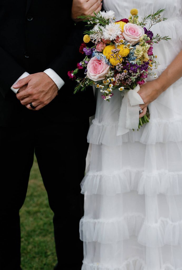 Close-up of a colorful wedding bouquet with pink roses, yellow flowers, greenery, and wildflowers.