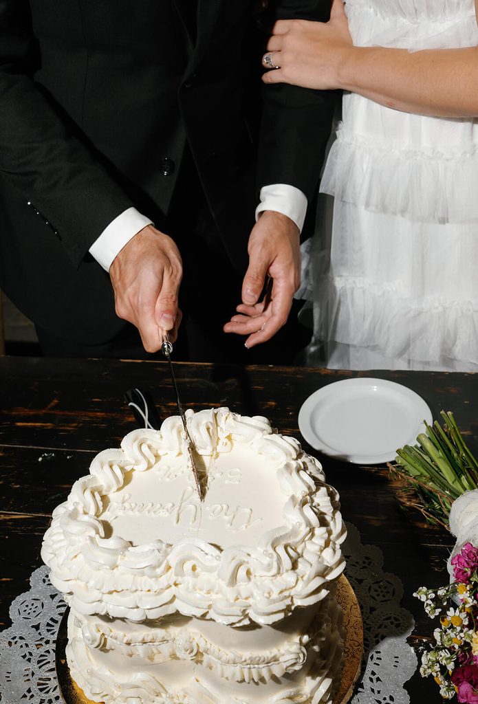 Bride and groom cutting a white vintage-style wedding cake together at their reception.