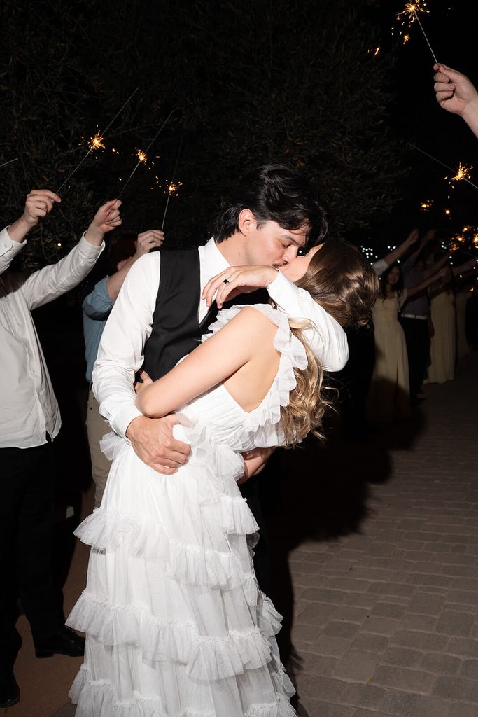 Groom dipping and kissing the bride during a nighttime sparkler exit.