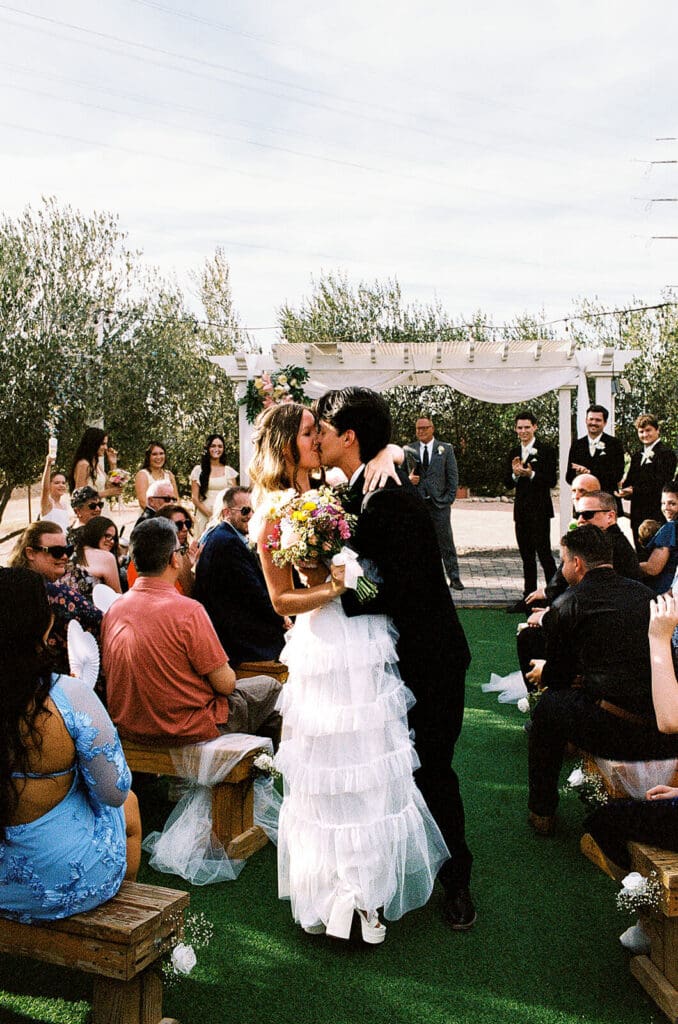 Newlyweds kissing as they walk back down the aisle after their outdoor wedding ceremony.