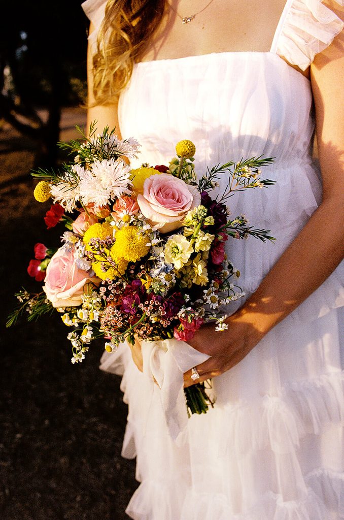 Close-up of a colorful bridal bouquet featuring pink roses, yellow flowers, white blooms, and greenery.